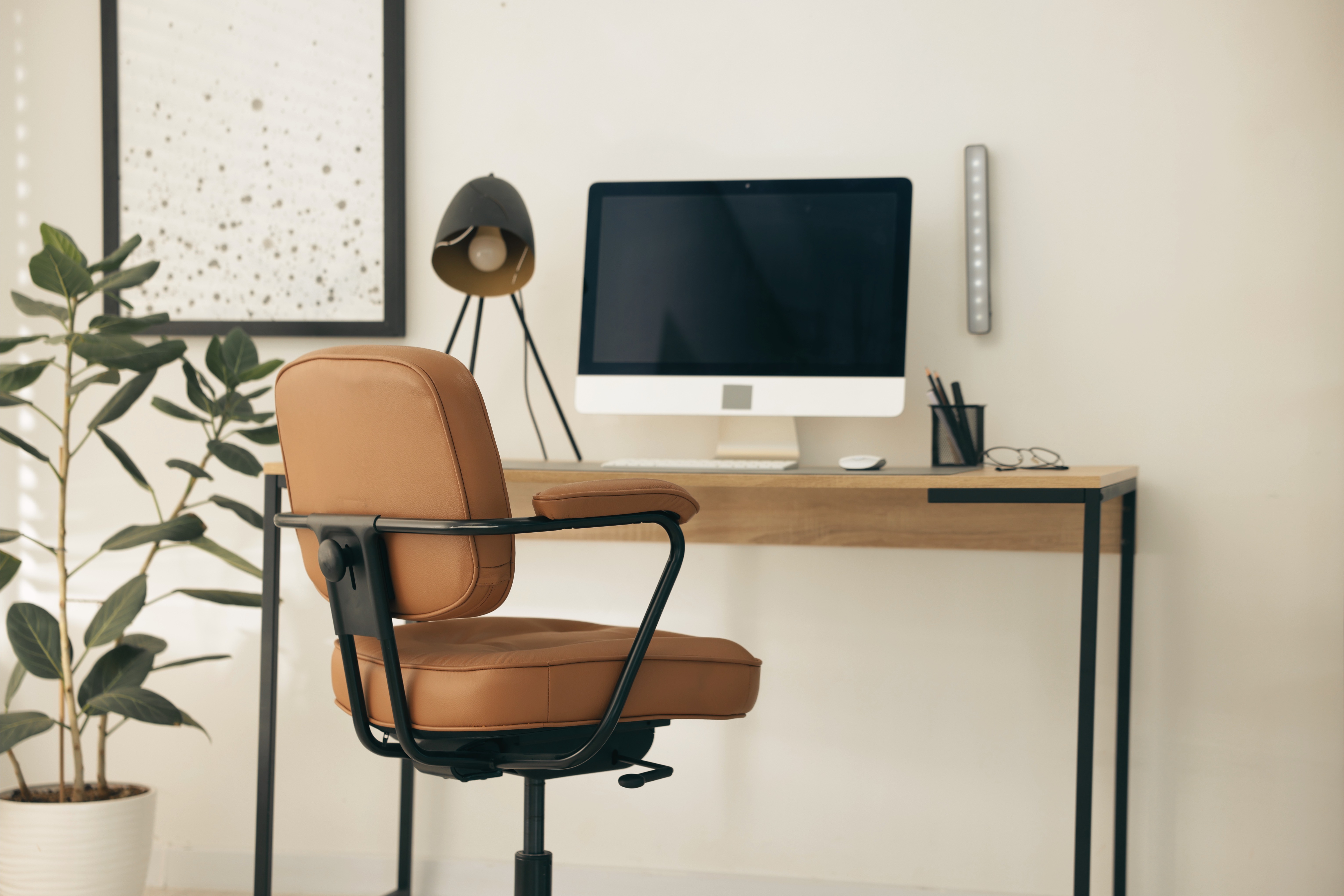 A clean home workspace with an adjustable desk chair, monitor, and lamp