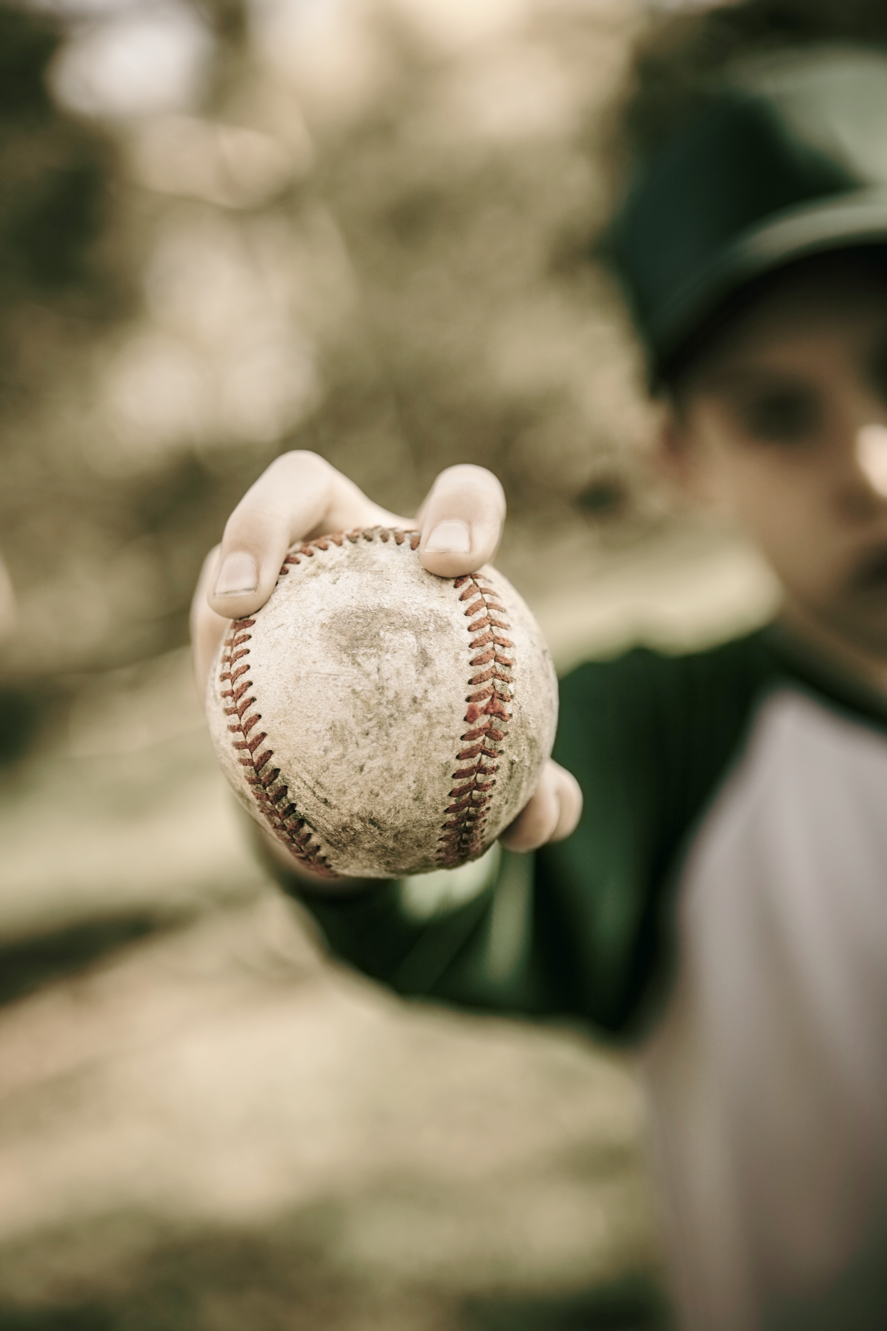 A young baseball player holding out a worn baseball toward the camera